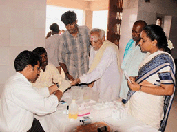 a village clinic with 4 people standing around a table attended by 2 medics who are performing tests 